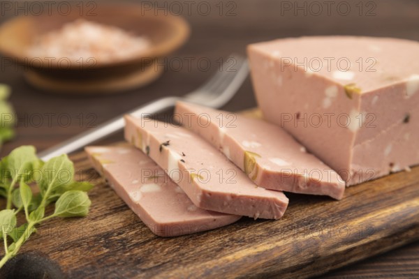 Mortadella sausage on wooden cutting board with pepper and herbs on brown wooden background. Side