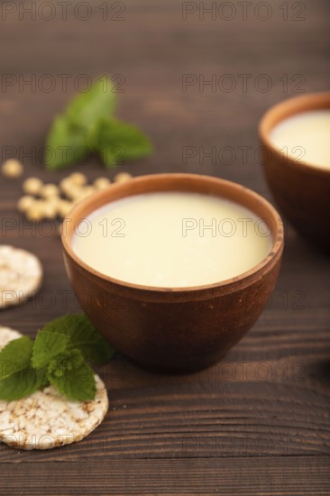 Organic non dairy banana and soy milk in clay cup on brown wooden background. Vegan healthy food