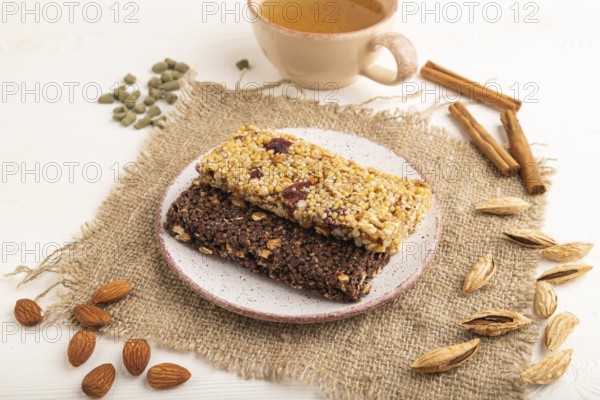 Granola bars with caramel, nuts, flakes in ceramic plate on white wooden background, beige linen