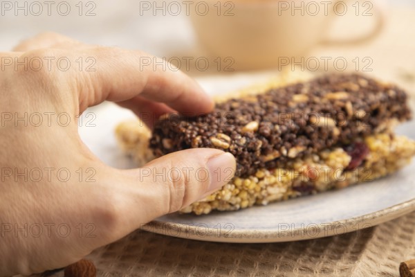 Granola bars with caramel, nuts, flakes in ceramic plate on brown concrete background with hand,