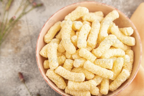 Corn flakes sticks with caramel in ceramic bowl on gray concrete background and orange linen