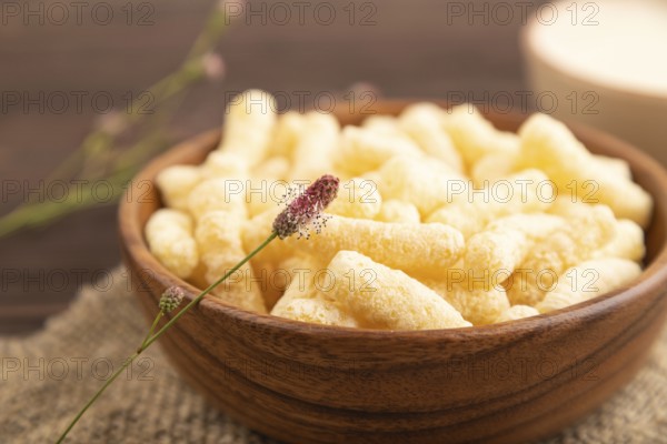 Corn flakes sticks with caramel in wooden bowl on brown wooden background and linen textile. Side
