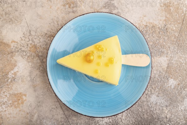 Yellow Cake pop with sprinkles on blue ceramic plate on brown concrete background, top view, flat