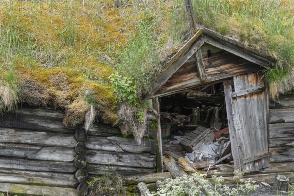 Abandoned, dilapidated wooden hut with grass roof in a green landscape against a mountain backdrop,