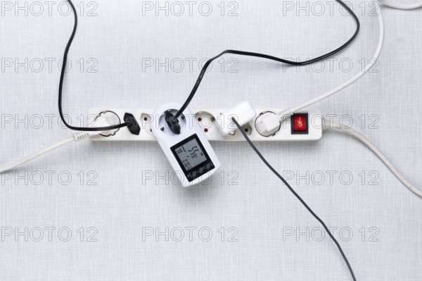 Top view of a power strip with on/off switch and various inserted plugs, cables and an electricity