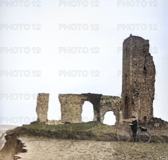 Colorised magic lantern slide of boy with bicycle standing by ruins of All Saints church, Dunwich,