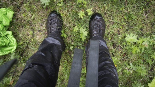 Blick auf nasse Wanderschuhe, Wanderhose und Gras von oben, regnerisches Wetter, Pilgerweg