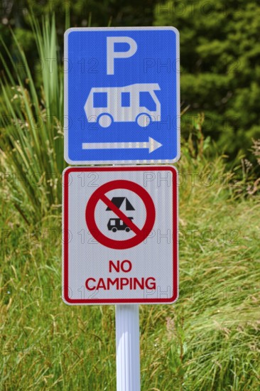 Ein Schild zeigt einen Parkplatz für Wohnmobile und ein Verbotsschild für Camping vor grüner