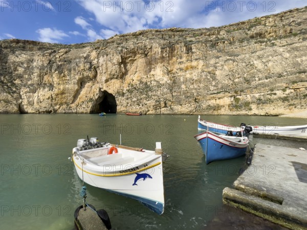 Moored excursion boat without tourists in inland sea of Gozo, in the background tunnel from passage