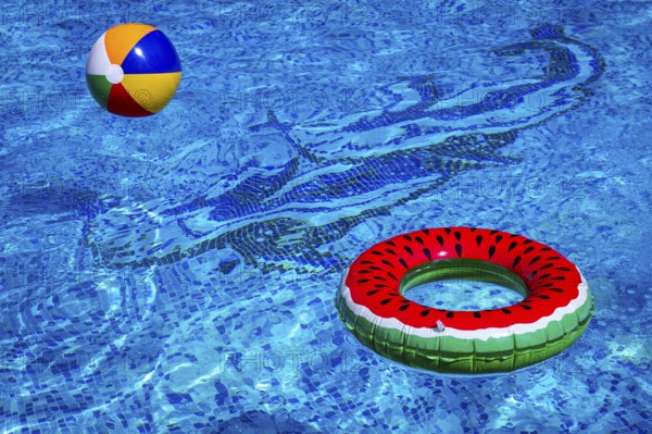 Colorful beach ball and watermelon circle, floating in the pool water, on a sunny summer day, no