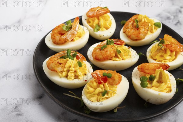 Boiled eggs stuffed with yolk and seasoned with mayonnaise, stuffed eggs with shrimp, on a black