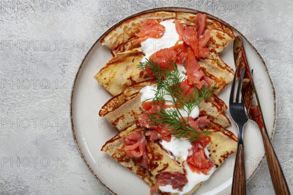 Delicious pancakes with salmon and sour cream, breakfast, on a plate, rustic style, with cutlery