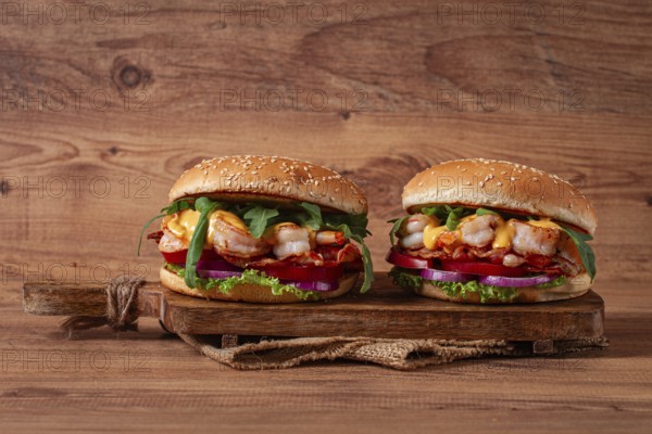 Two shrimp burgers and buns with sesame seeds, bacon, lettuce, tomatoes and onions, on a wooden