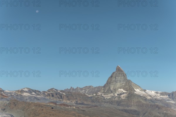 The iconic Matterhorn stands high above a clear evening sky illuminated by a bright moon. This