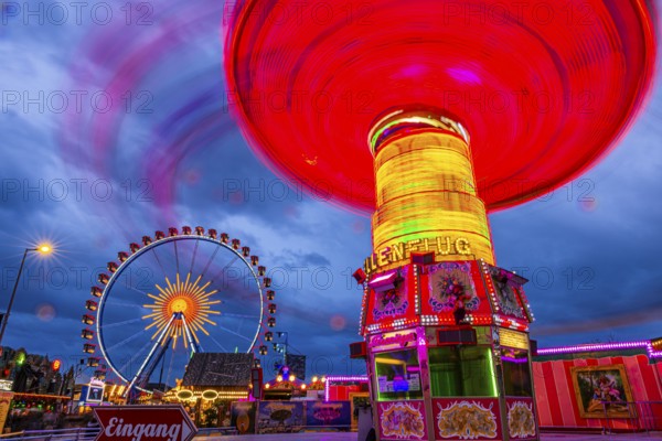 Illuminated chain carousel in motion, behind the Ferris wheel at standstill, Festwiese,