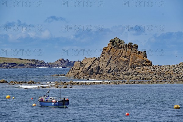 Rocky coastal landscape with a small boat and colourful buoys under a blue sky, Isles of Scilly,