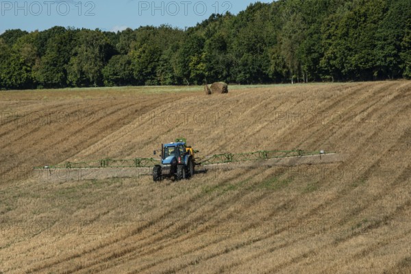 Tractor spreading fertilizer on harvested stubble field in Ystad municipality, Skåne county,