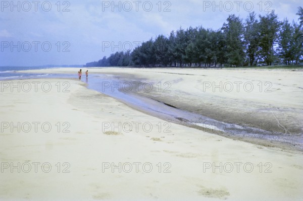 Men walking on sandy beach south of estuary, Rompin, East coast, Pahang, Malaya, Malaysia, south