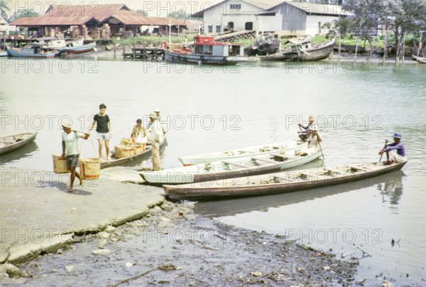 Canoes bringing fish to market, ice and fish packing factories, East coast, Mersing, Johor, Malaya,