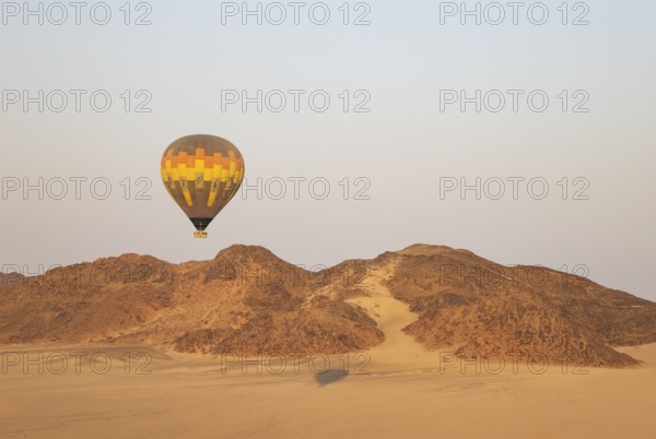 The hot-air balloon above an arid plain and isolated mountain ridges at the edge of the Namib