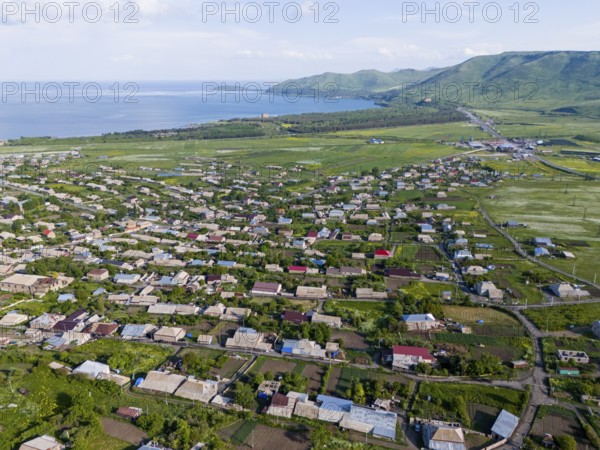 Vast landscape with houses and green fields by the sea and mountains in the distance, aerial view,