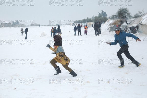 Displaced Syrian children playing in the snow near their tents inside a refugee camp during winter.