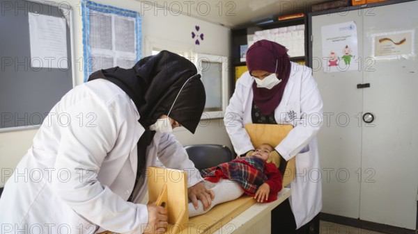 A doctor examining a refugee child for malnutrition in the camp using weight and height measurement