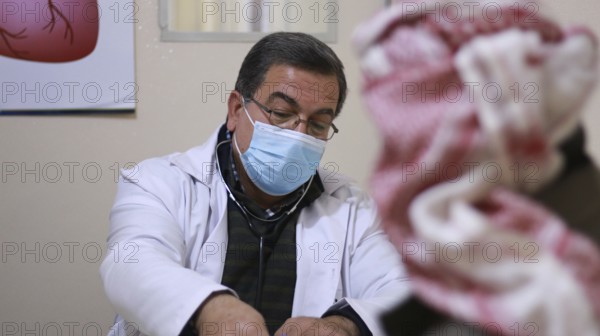 A Syrian doctor wearing a protective mask consults with a displaced patient inside a medical clinic
