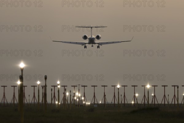 Executive business jet passenger aircraft landing over runway lights at sunset, London Stansted