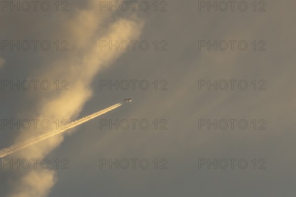 Jet passenger aircraft with a vapour trail or contrail flying in a sky with clouds, England, United