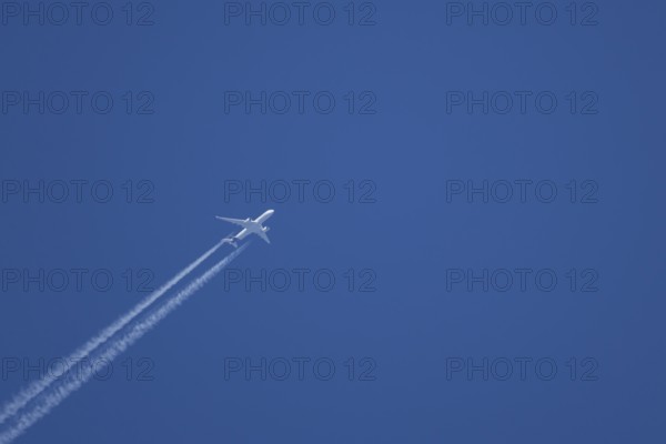 Jet passenger aircraft with a vapour trail or contrail flying in a blue sky, England, United