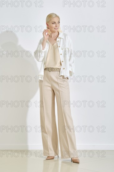 A woman dressed in a cream top and stylish beige trousers strikes a confident pose in a minimalist