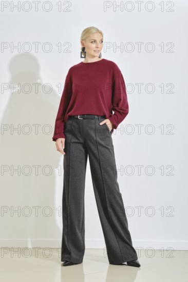 A fashion model stands confidently in a minimalist studio, wearing a maroon sweater and