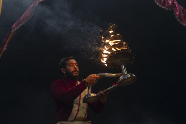 Hindu priest performing the Aarti ritual, holding a burning oil lamp, at the Ganges, Bangali Tola,