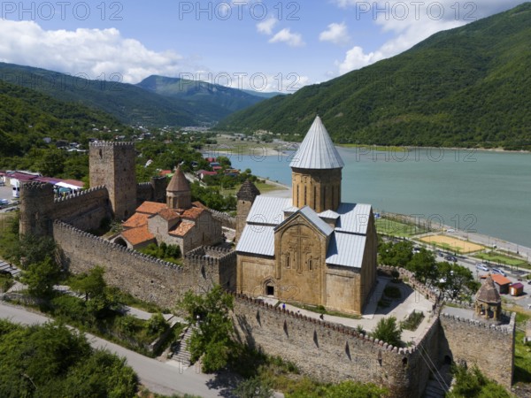 Historic fortress above a reservoir, surrounded by green hills in an idyllic setting, aerial view,