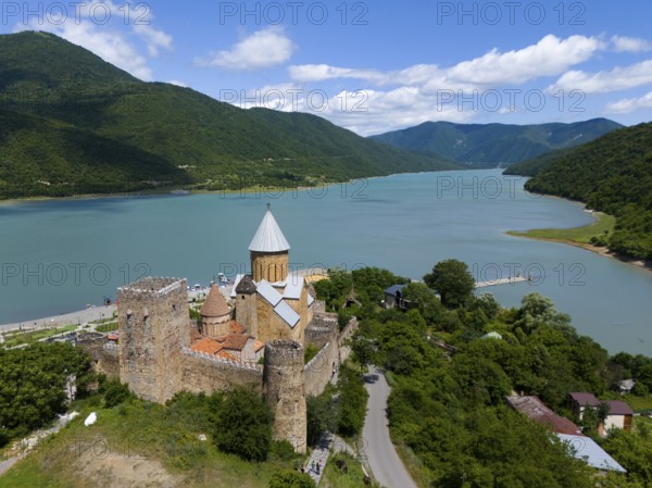 Medieval castle on the river surrounded by green mountains under a cloudy sky, aerial view, Ananuri