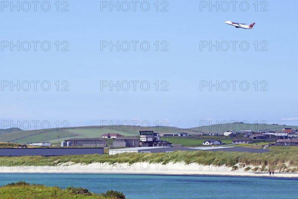 Aeroplane taking off over coast with hangars and green land, Sumburgh Head, Shetland Islands,