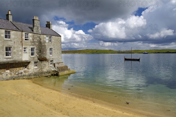 Old stone cottage on quiet loch shore with sandy beach and passing boat under cloudy sky, Murder in