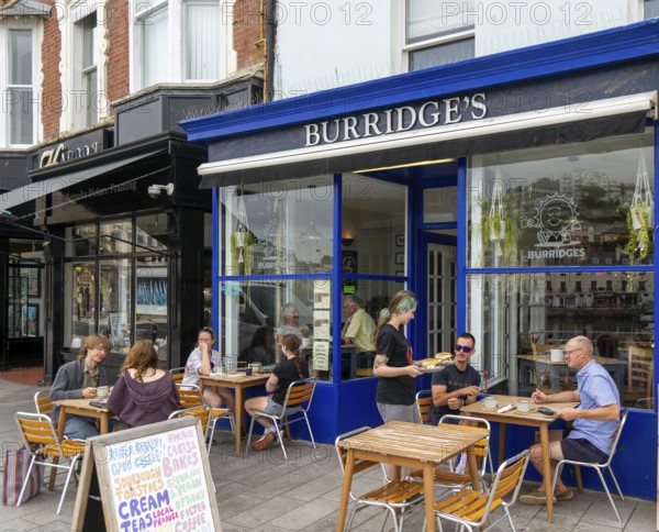 People sitting at tables on pavement outside Burridges cafe, Victoria Parade, Torquay, Devon,