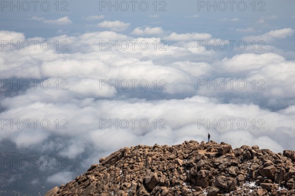 Colorado Springs, Colorado - A man stands on the rocks just below the summit of Pikes Peak, a 14,