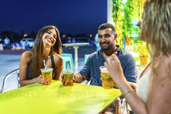 Three friends are laughing and chatting while enjoying refreshing beverages at a vibrant outdoor