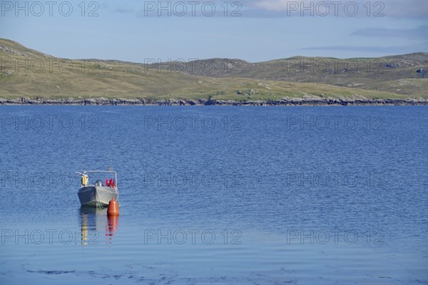 Lonely boat next to buoy on calm water, hilly landscape behind under clear sky, Hillswick,
