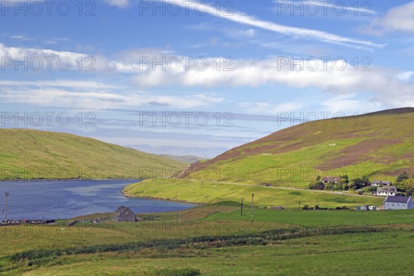 Green hilly landscape with a river and scattered houses under a blue, slightly cloudy sky, Voe,