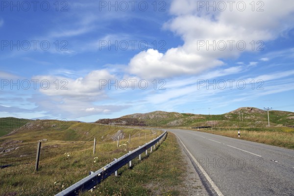Empty road winds through hilly landscape under blue sky with clouds, Eshaness, Shetland Islands,
