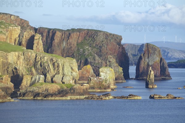 Coastal landscape with high cliffs lined with rocks and wind turbines in the background, Hillswick,