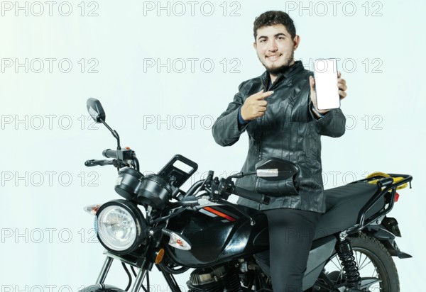 Young motorcyclist sitting on his motorcycle showing cell phone screen isolated. Male biker on his