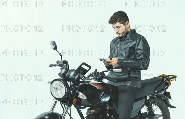 Young motorcyclist using his cell phone while sitting on his motorcycle, isolated. Male biker on a