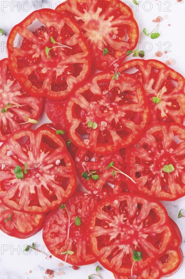 Freshly sliced ripe tomatoes arranged on a marble surface with microgreens and sea salt for a