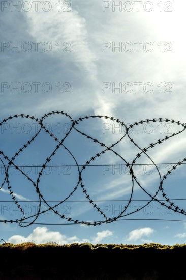 A barbed wire fence stretches across the foreground, silhouetted against a clear blue sky with