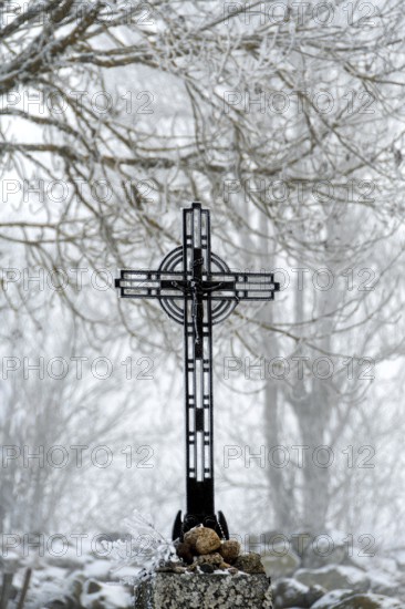 A beautiful wayside cross stands tall in winter with snow blanketing the landscape of the Aubrac